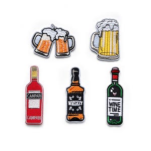 Può includere: Cinque toppe ricamate da stirare con diverse bevande alcoliche. Le toppe includono due boccali di birra che brindano, un bicchiere di birra, una bottiglia di Campari, una bottiglia di whisky e una bottiglia di vino con il testo "Wine Time".