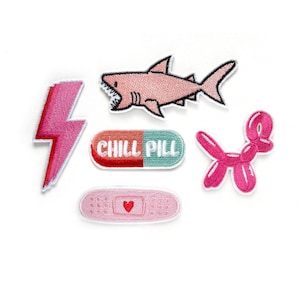 Puede incluir: Seis parches bordados para planchar en rosa, rojo y azul. Los parches incluyen un rayo, un tiburón, una píldora con el texto "CHILL PILL", un animal de globo y una venda con un corazón.