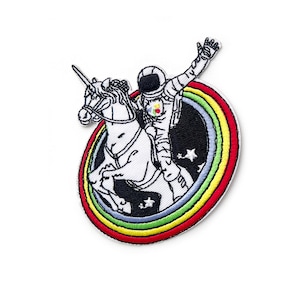 Può includere: Una toppa ricamata con un unicorno bianco con un arcobaleno intorno. Un astronauta è in sella all'unicorno. L'astronauta indossa una tuta spaziale bianca con una toppa rossa, gialla e blu sul petto.