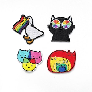 Könnte beinhalten: Vier gestickte Bügelbilder mit einer Gans, die eine Regenbogenflagge hält, einer schwarzen Katze mit Regenbogen-Sonnenbrille, drei bunten Katzen, die übereinander gestapelt sind, und einer roten Katze mit einer gelben, grünen und blauen Katze darin.