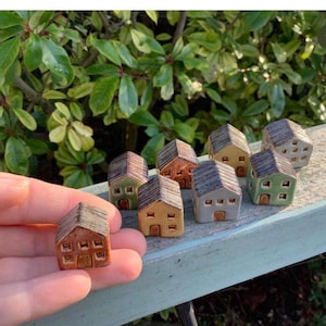 May include: A collection of miniature ceramic houses in various shades of green, brown, and grey. The houses have small windows and doors, and some have textured roofs.
