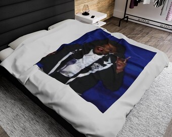 May include: A white bedspread with a blue background featuring a person in a black and white outfit making a peace sign.