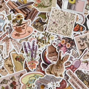 May include: A selection of vintage-style stickers with floral designs, a teacup with flowers, a brown rabbit, butterflies, and lavender. The stickers are in various shapes and sizes, with a muted colour palette of beige, pink, and brown.