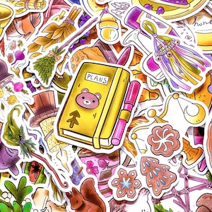 Può includere: Una collezione di adesivi colorati con vari disegni. Un taccuino giallo con la parola "PLANS" e un'illustrazione di orso è accanto a una penna rosa. Altri adesivi includono una scopa, uno scoiattolo e un biscotto di pan di zenzero.