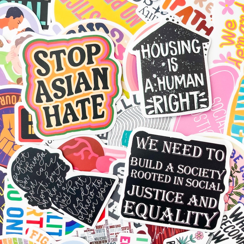 May include: A collection of colorful stickers with various social justice messages. One sticker reads "STOP ASIAN HATE" in bold black letters with a pink, orange, and green border. Other stickers include "HOUSING IS A HUMAN RIGHT" and "WE NEED TO BUILD A SOCIETY ROOTED IN SOCIAL JUSTICE AND EQUALITY."