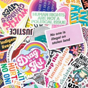 May include: A collection of colorful stickers with various text and graphic designs. The stickers feature phrases like "Human Rights Are Not a Political Issue," "Drag is Art," and "No one is illegal on stolen land."