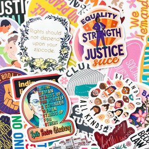 May include: A collection of colorful stickers with various designs and text. Some stickers feature phrases like "Equality Strength Justice" and "Rights should not depend upon your zipcode." Other stickers have illustrations of people and flowers.