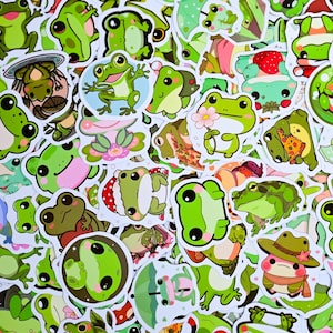 Puede incluir: Una colección de pegatinas de ranas coloridas en varias poses y diseños. Las pegatinas presentan tonos de verde, con algunas ranas sosteniendo flores, usando sombreros o con otros accesorios. Las pegatinas están sobre un fondo blanco.