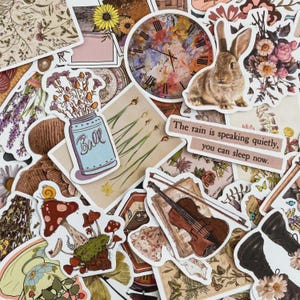 May include: A selection of vintage-style stickers featuring a rabbit, clock, flowers, a mason jar, a violin, and mushrooms. The text "The rain is speaking quietly, you can sleep now" is visible on one of the stickers.