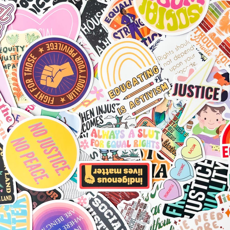 May include: A collection of colorful stickers with various designs and text. The stickers feature phrases like "No Justice, No Peace," "Educating is Activism," and "Indigenous Lives Matter." Other designs include a raised fist, a rainbow, and hearts.