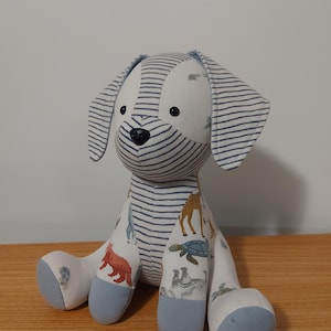 Peut inclure: Une peluche en forme de chien faite à la main. Le corps est fait de tissu à rayures bleues et blanches, tandis que les pattes sont ornées d'imprimés d'animaux. Les pattes et l'intérieur des oreilles sont bleu clair.