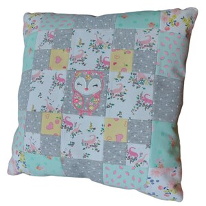 May include: A patchwork cushion with a light green, grey, white, and yellow colour scheme. The cushion features a pink and white owl appliqué in the centre.
