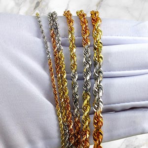 May include: A set of five gold, silver, and rose gold rope chains of varying thicknesses. The chains are displayed on a white surface.