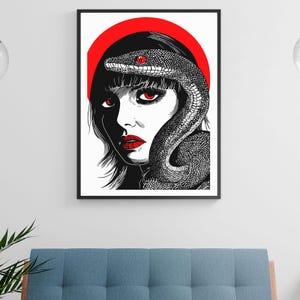 Könnte beinhalten: Schwarz-Weiß-Kunstdruck mit einer Frau mit roten Augen und Lippen, einer Schlange, die sich um ihren Kopf windet, und einem roten Heiligenschein. Das Kunstwerk ist in einem schwarzen Rahmen gerahmt.