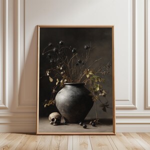 May include: A framed still life print featuring a dark gray vase filled with dried black seed pods and branches, with green and yellow leaves. A human skull and dark berries are at the base of the vase. The background is a dark, moody color.