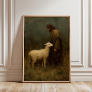 Puede incluir: Una impresión vintage enmarcada representa una figura con túnica marrón y barba larga, de pie junto a un cordero blanco en un campo de hierba alta. La obra de arte tiene una paleta de colores suaves y apagados.
