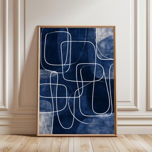 May include: Abstract art print featuring a navy blue background with white, continuous line drawings. The artwork is framed in a natural wood tone, creating a modern and minimalist aesthetic. The design incorporates geometric shapes and flowing lines.
