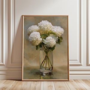 May include: A framed oil painting depicting a bouquet of white hydrangea flowers in a clear glass vase. The flowers have textured petals and green stems visible through the glass. The background is a soft, muted blend of beige and light blue tones.