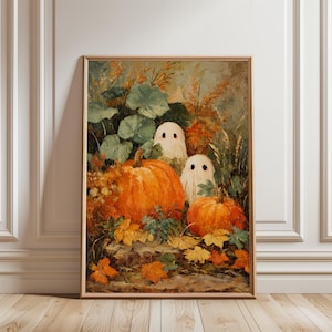 Może przedstawiać: Oprawiony wydruk artystyczny na Halloween przedstawiający dwie białe postacie duchów z czarnymi oczami w kropki, otoczone pomarańczowymi dyniami, zielonymi liśćmi i jesiennymi liśćmi. Grafika jest w drewnianej ramie, w stylu vintage i rustykalnym.