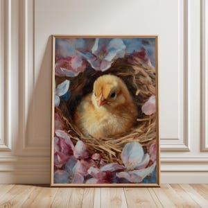 May include: A framed painting of a yellow chick nestled in a woven nest, surrounded by pink and white blossoms. The artwork has a soft, painterly style with a focus on the chick's fluffy feathers and the delicate petals.