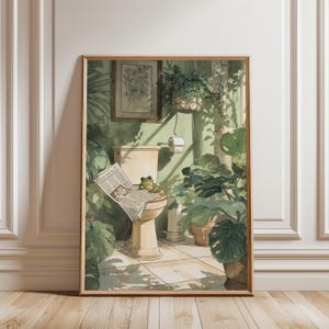Op de afbeelding: Een ingelijste kunstdruk toont een grillige badkamerscène. Een kikker zit op een toilet en leest een krant, omringd door weelderige groene planten. De muren zijn zachtgroen geschilderd en het kunstwerk heeft een vintage aquarel stijl.