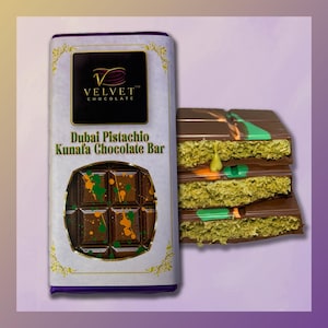 May include: A chocolate bar with a white wrapper and gold accents. The wrapper says "Velvet Chocolate" and "Dubai Pistachio Kunafa Chocolate Bar". The chocolate bar is broken into pieces, revealing a green and orange filling.