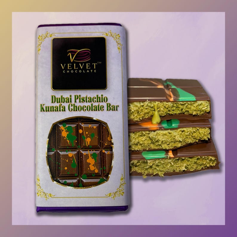 May include: A chocolate bar with a white wrapper and gold accents. The wrapper says "Velvet Chocolate" and "Dubai Pistachio Kunafa Chocolate Bar". The chocolate bar is broken into pieces, revealing a green and orange filling.