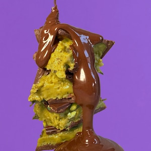 May include: A stack of chocolate-covered cookie dough bites drizzled with melted chocolate. The bites are layered with chocolate pieces and green sprinkles.