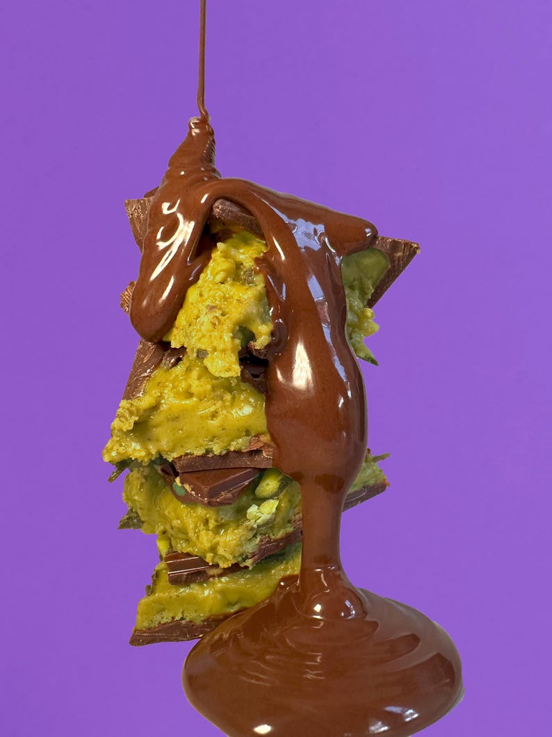 May include: A stack of chocolate-covered cookie dough bites drizzled with melted chocolate. The bites are layered with chocolate pieces and green sprinkles.