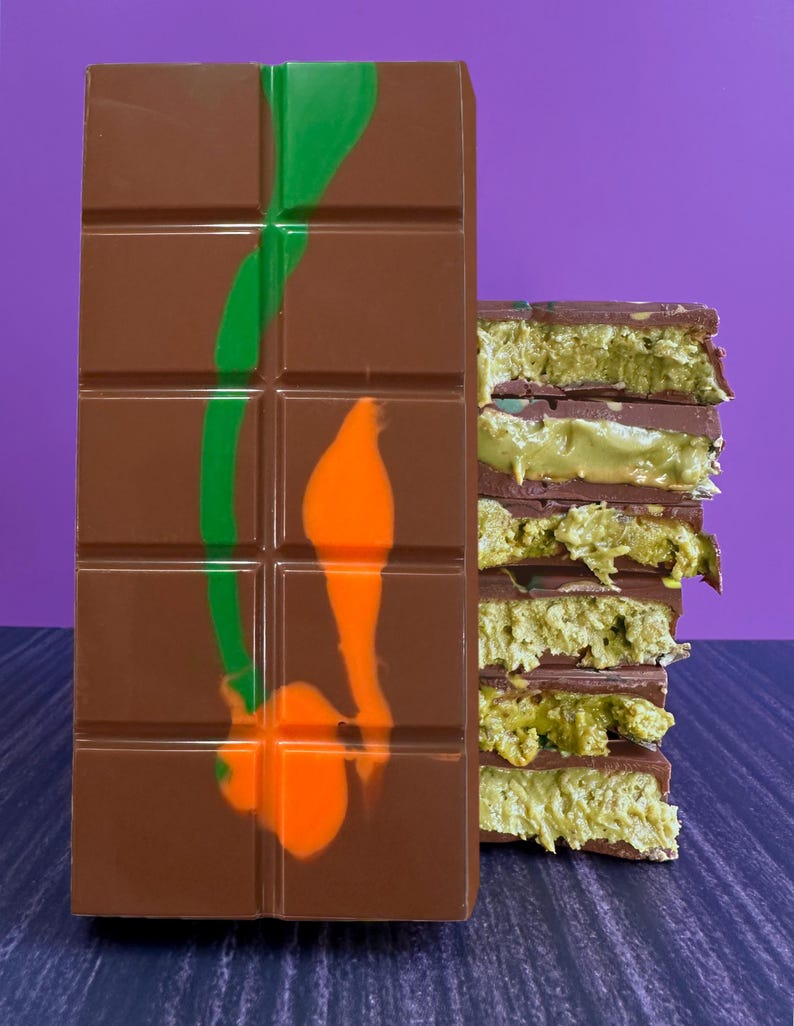May include: A chocolate bar with green and orange swirls on the front. The bar is broken into squares. A stack of chocolate-covered layers with green filling is shown on the right.