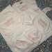 May include: A white baby clothing set with pink trim, featuring a blanket, bib, hat, and a long-sleeved gown. Each item is embroidered with a floral bow design and the name "Ellie Rae" in pink script. The set is designed for newborns.