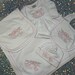 May include: A white baby clothing set featuring a blanket, dress, bib, and hat. Each item is embroidered with a pink bow and the name "Ellie Rae". The set has pink trim.