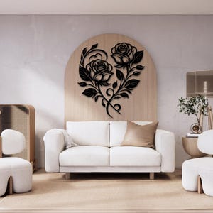 Peut inclure: Décoration murale en métal noir représentant deux roses avec des détails floraux complexes, formant une forme de cœur. L'œuvre d'art est montée sur un mur brun clair au-dessus d'un canapé blanc.