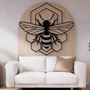 May include: A black metal bee wall art piece. The bee is centered on a wooden arched background, with a honeycomb design behind it. The bee has detailed wings and body stripes. The artwork is displayed above a white couch with a brown pillow.