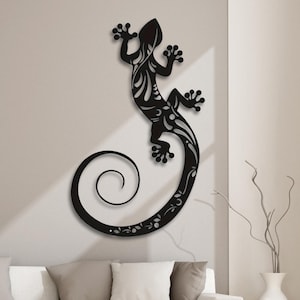 Puede incluir: Arte de pared de metal negro con un gecko estilizado con una cola enroscada. El gecko está detallado con intrincados patrones florales.