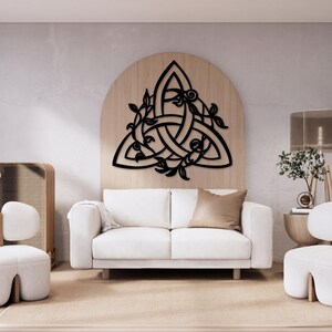 May include: A black metal wall decor featuring a Celtic knot design with intricate floral details. The design is in the shape of a triangle and is mounted on a light wood background.