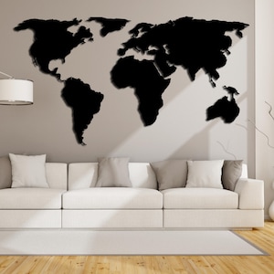 May include: A black world map wall decor with a 3D effect, mounted on a light gray wall above a white couch with pillows.
