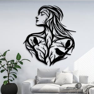 Könnte beinhalten: Schwarze Metall-Wandkunst, die das Profil einer Frau mit fließendem Haar und einem baumartigen Design zeigt, das ihren Körper bildet. Drei Vögel sitzen auf den Ästen. Das Kunstwerk ist an einer weißen Wand befestigt.
