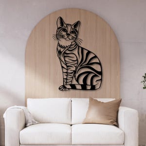 May include: Black metal wall decor featuring a stylized silhouette of a cat sitting with its tail curled around its legs. The cat has a striped pattern and a friendly expression.