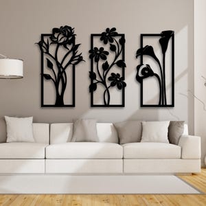 May include: Three black metal wall decor pieces featuring floral designs. Each piece is framed with a rectangular border and features a different floral design. The designs include a rose, a cluster of flowers, and a calla lily.