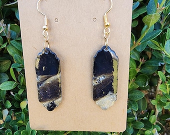 May include: A pair of gold earrings with black and silver rectangular shaped pendants. The pendants have a marbled design.