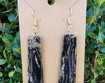 May include: A pair of black and gold dangle earrings with a marbled pattern. The earrings are hanging on a brown card.