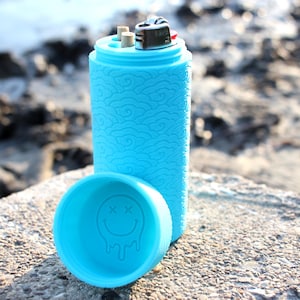 May include: A light blue lighter case with a cloud pattern and a smiley face on the lid. The case is open and the lighter is inside.
