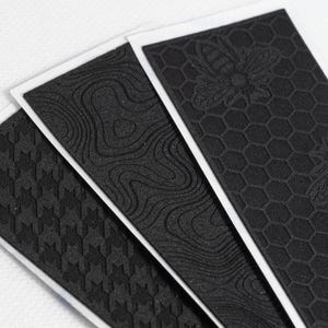 May include: Three rectangular black adhesive grip tapes with white backing. The left features a houndstooth pattern, the center has a topographic map design, and the right displays a honeycomb pattern with a bee icon. Text reads @STREETCORN.FL.