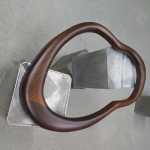 May include: A dark brown wooden frame with a curved, irregular shape. The frame is resting on a gray surface.