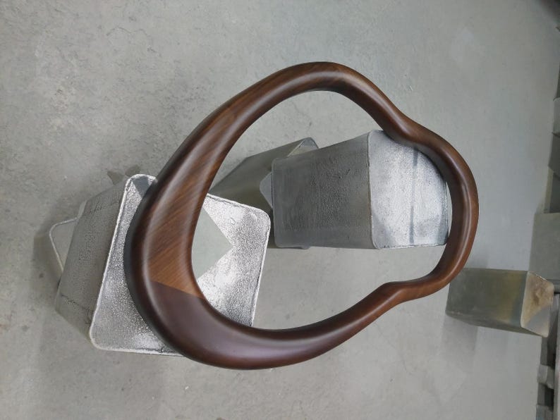 May include: A dark brown wooden frame with a curved, irregular shape. The frame is resting on a gray surface.