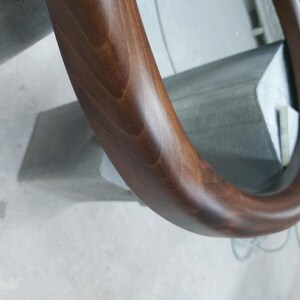 May include: A close-up of a dark brown wooden handrail with a smooth, polished finish. The handrail is curved and has a rounded edge.
