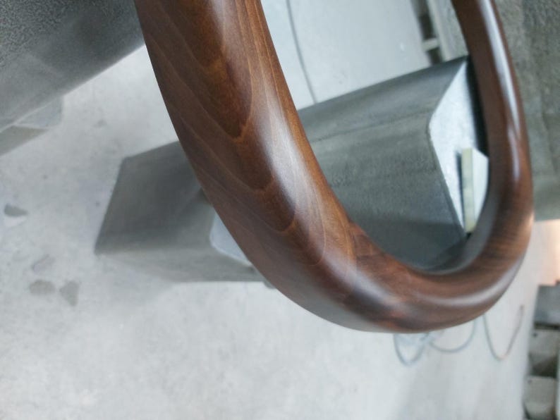 May include: A close-up of a dark brown wooden handrail with a smooth, polished finish. The handrail is curved and has a rounded edge.