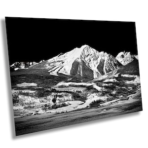 Pode incluir: Uma fotografia a preto e branco de uma cordilheira coberta de neve. As montanhas estão cobertas de neve e o céu está escuro. A imagem foi tirada de longe, olhando para as montanhas.