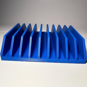 May include: A vibrant blue desk organizer with multiple vertical slots. The organizer is made of a solid material and has a rectangular base. The slots are evenly spaced, creating a structured and organized appearance.